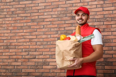 Food delivery courier holding paper bag with products near brick wall. Space for text