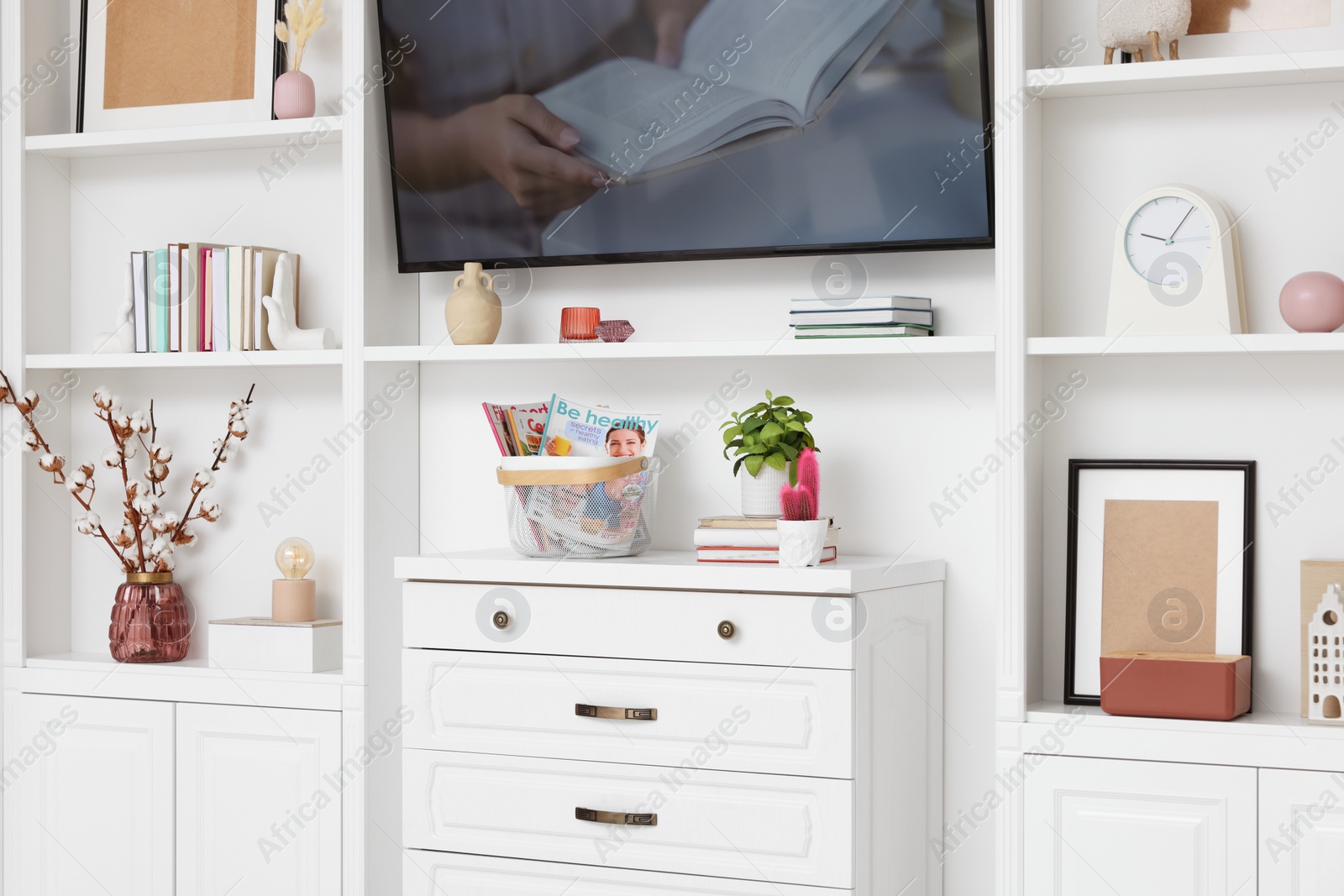 Photo of TV and shelves with different decor in room. Interior design