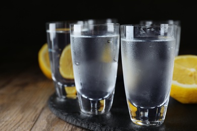 Vodka in shot glasses and lemons on wooden table, closeup