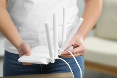 Photo of Woman connecting cable to Wi-Fi router at table indoors, closeup