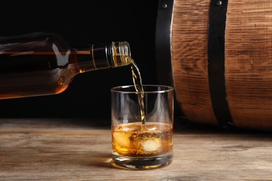 Photo of Pouring whiskey from bottle into glass on wooden table