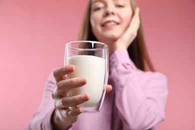 Cute woman with milk mustache holding glass of tasty dairy drink on pink background, closeup