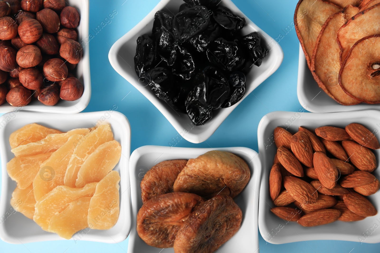 Photo of Bowls with dried fruits and nuts on light blue background, flat lay