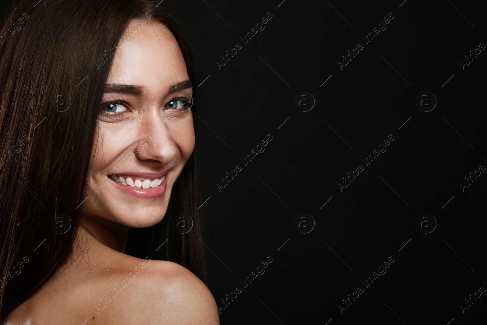 Photo of Portrait of pretty young woman with gorgeous chestnut hair and charming smile on black background, space for text