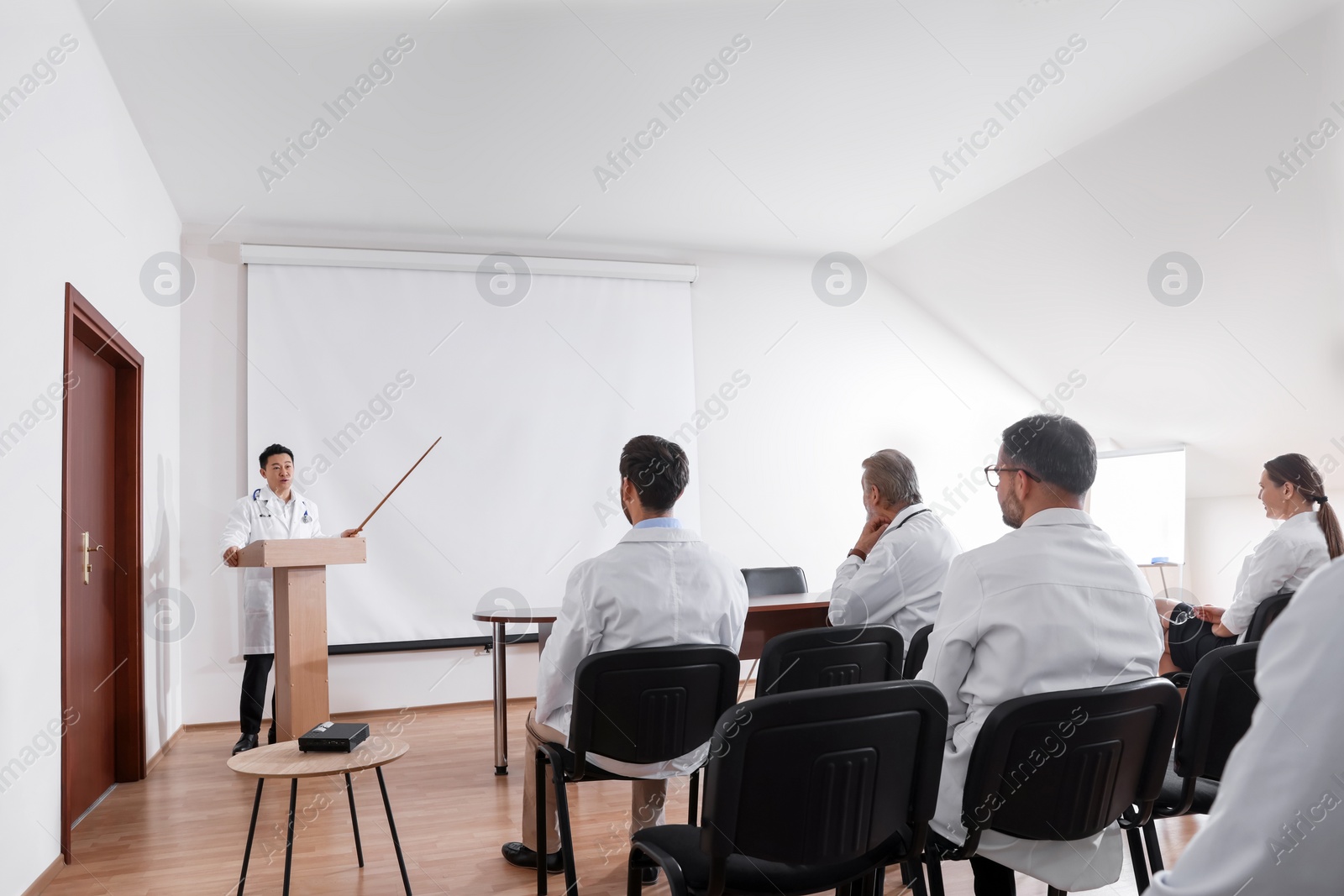 Photo of Doctor giving lecture in conference room with projection screen