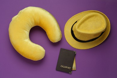 Photo of Yellow travel pillow, hat and passport with credit card on purple background, flat lay