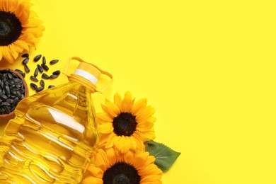 Photo of Bottle of cooking oil, sunflowers and seeds on yellow background, flat lay. Space for text