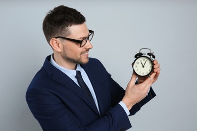 Photo of Happy businessman holding alarm clock on grey background. Time management