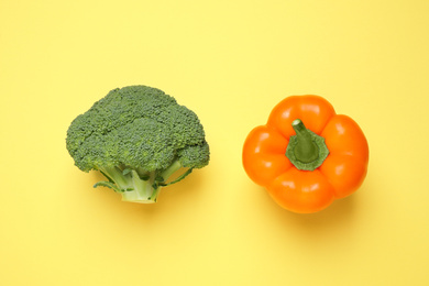 Fresh broccoli and bell pepper on yellow background, flat lay