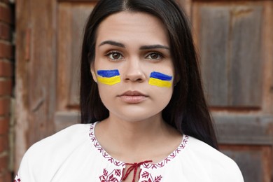 Photo of Young beautiful woman with drawings of Ukrainian flag on face near wooden door
