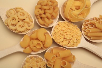 Different types of pasta in spoons on beige background, flat lay