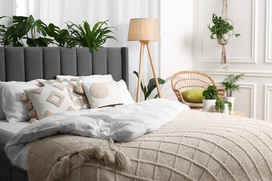 Photo of Comfortable bed, wicker armchair, lamp and beautiful houseplants in room. Bedroom interior
