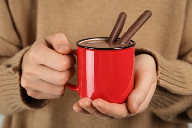 Woman holding cup of delicious hot chocolate with cocoa sticks, closeup