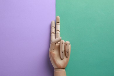 Wooden mannequin hand on color background, top view