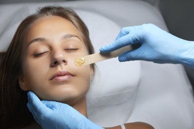 Young woman undergoing hair removal procedure on face with sugaring paste in salon