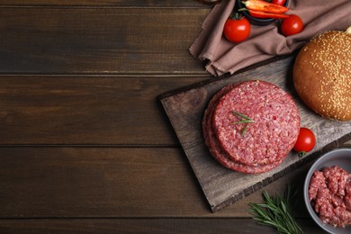 Photo of Raw hamburger patties with rosemary and tomatoes on wooden table, flat lay. Space for text