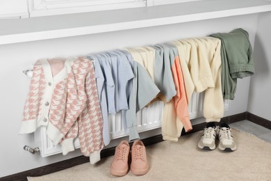 Photo of Heating radiator with clothes and shoes in room