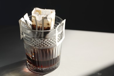 Photo of Glass with drip coffee bag on light grey table, closeup. Space for text