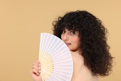 Woman holding hand fan on beige background. Space for text