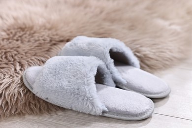 Grey soft slippers on light wooden floor at home, closeup