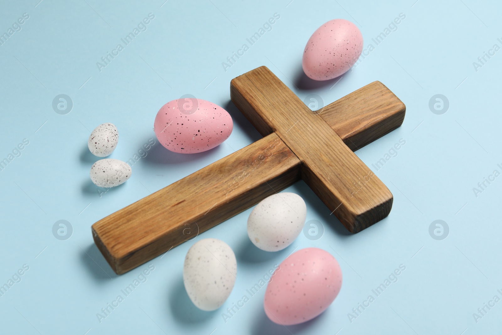 Photo of Wooden cross and painted Easter eggs on light blue background