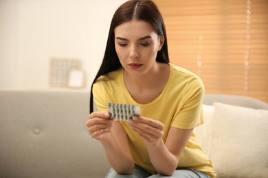 Photo of Young woman holding package of pills at home