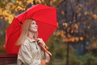 Woman with umbrella sitting on bench in autumn park. Rainy day