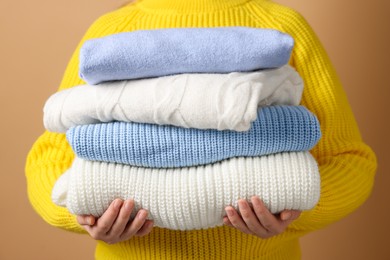 Photo of Woman with stack of casual sweaters on light brown background, closeup