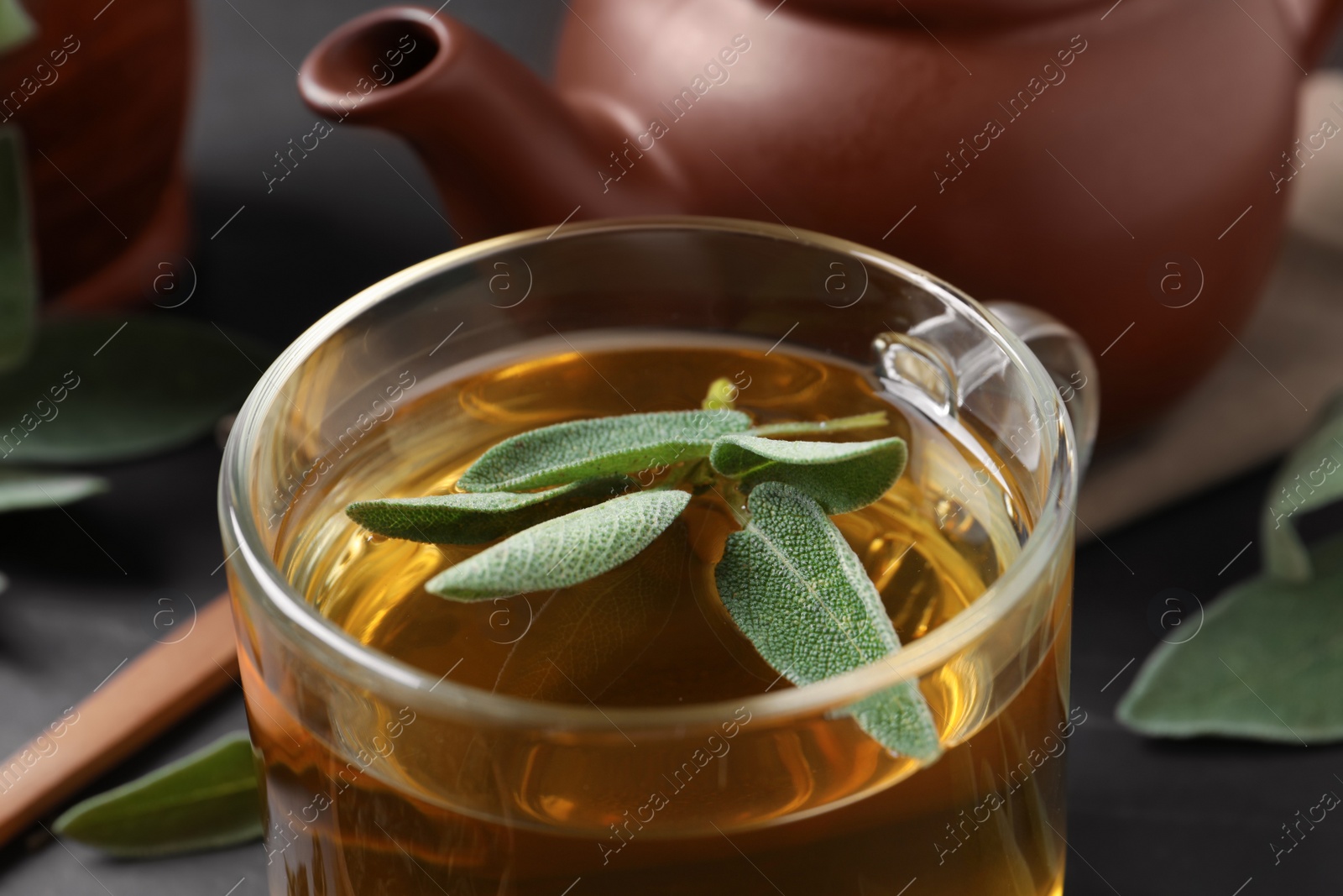 Photo of Cup of aromatic sage tea with fresh leaves on table, closeup