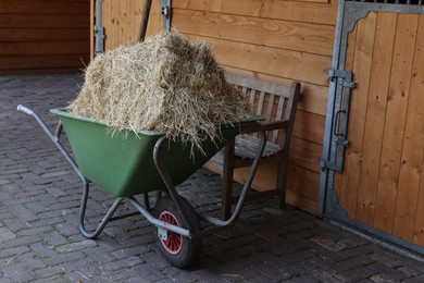 Wheelbarrow with hay near wooden stable outdoors