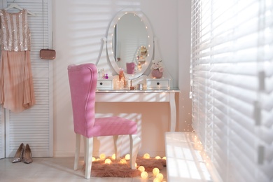 Elegant dressing table with lights and pink chair in stylish room interior