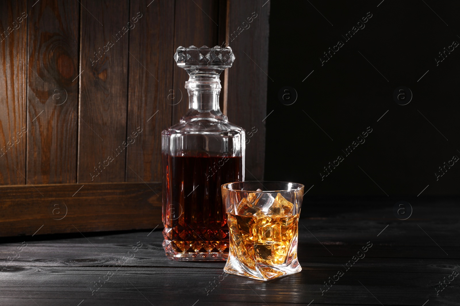 Photo of Whiskey with ice cubes in glass and bottle on black wooden table
