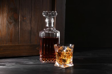 Whiskey with ice cubes in glass and bottle on black wooden table