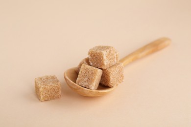 Photo of Brown sugar cubes and spoon on beige background, closeup