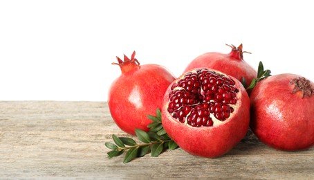 Fresh pomegranates and green leaves on wooden table against white background, space for text