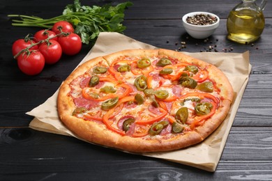 Photo of Delicious pizza Diablo and ingredients on black wooden table