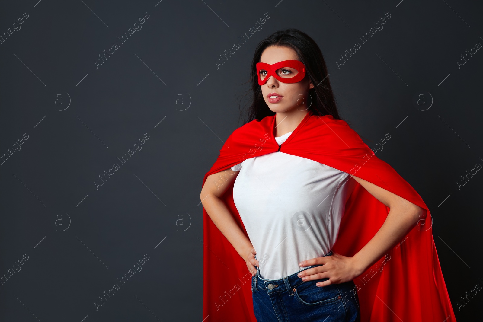 Photo of Confident young woman wearing superhero cape and mask on grey background, space for text