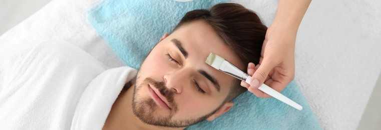 Cosmetologist applying mask on client's face in spa salon, above view. Banner design