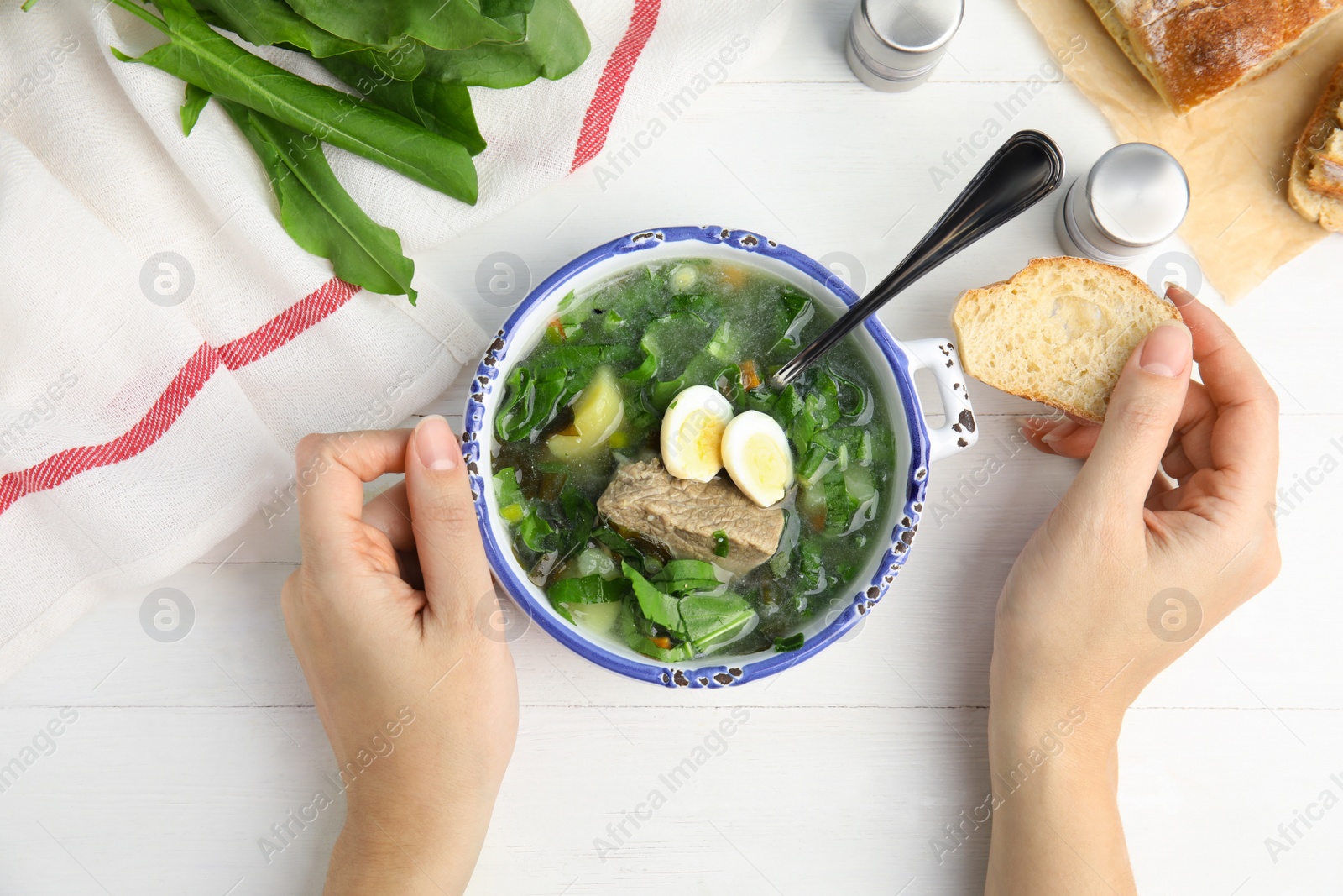 Photo of Woman eating delicious sorrel soup with meat and eggs at white wooden table, top view