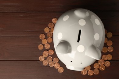 Photo of Ceramic piggy bank and coins on wooden table, flat lay. Space for text