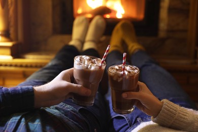 Photo of Couple with glasses of hot cocoa near fireplace at home, closeup
