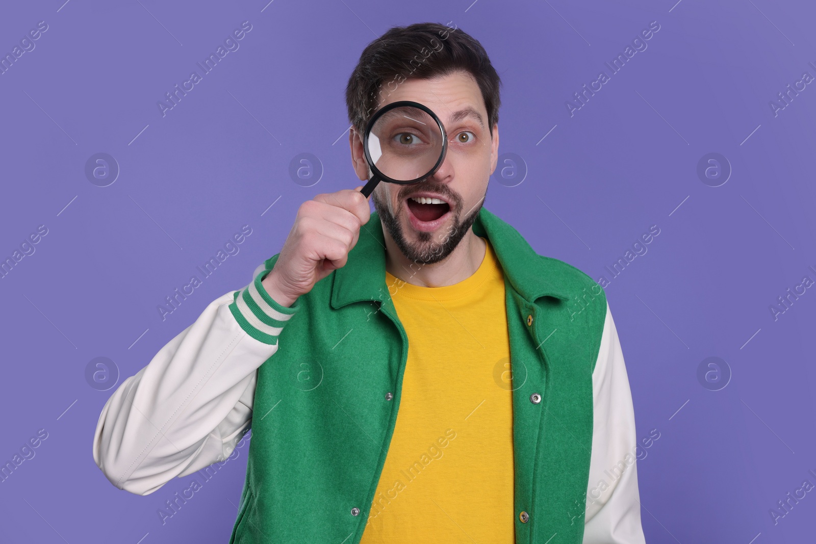 Photo of Emotional man looking through magnifier glass on purple background