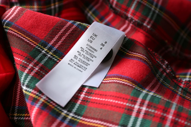 Photo of Clothing label with size and content information on red plaid garment, closeup