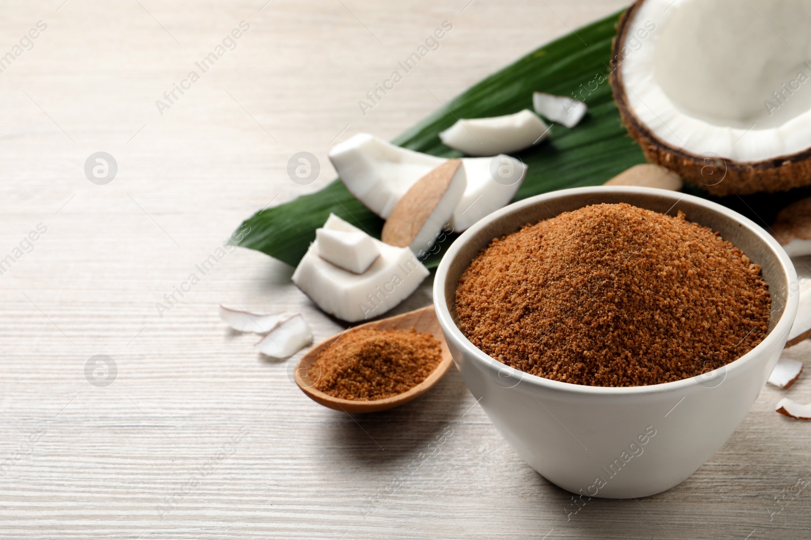 Photo of Natural coconut sugar in bowl on white wooden table, space for text