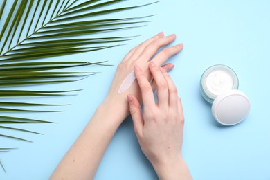 Photo of Woman applying hand cream on light blue background, top view