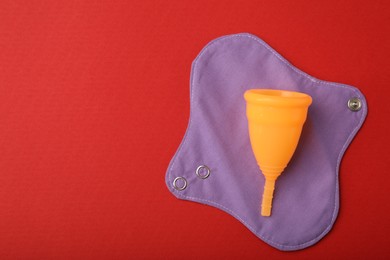 Photo of Menstrual cup and cloth pad on red background, top view. Space for text