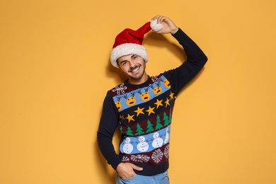 Young man in Christmas sweater and hat on color background