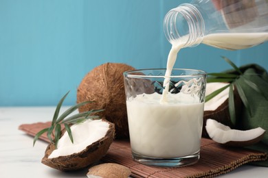 Pouring delicious coconut milk into glass at white marble table, closeup