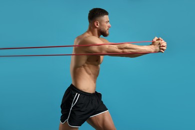Photo of Muscular man exercising with elastic resistance band on light blue background