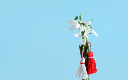 Traditional martisor and beautiful snowdrops on light blue background, space for text. Symbol of first spring day